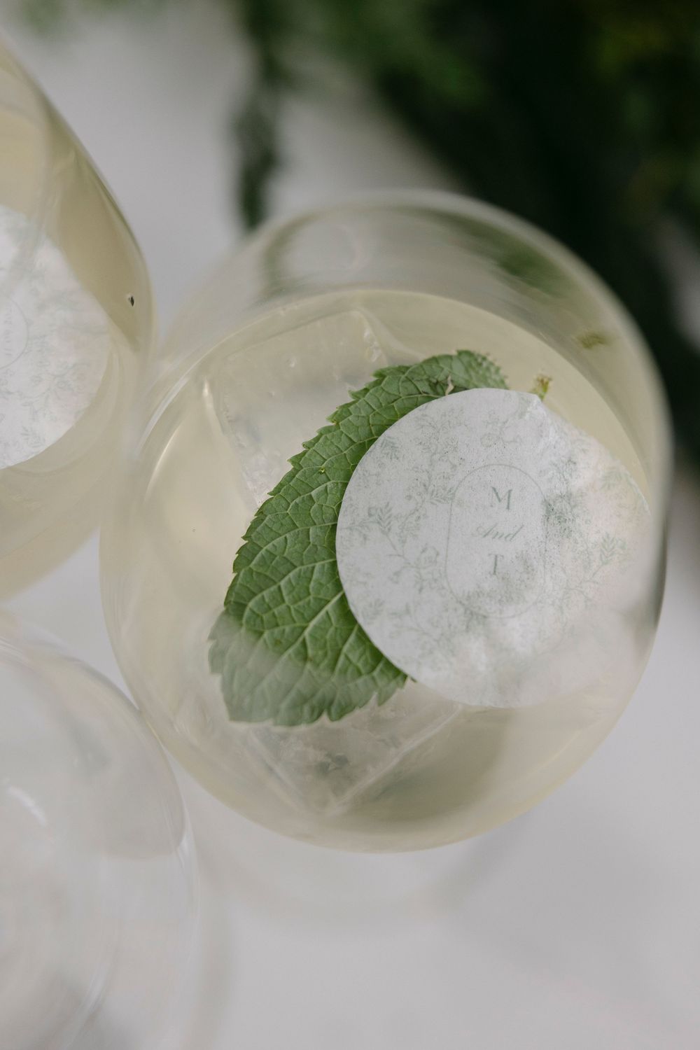 Close-up of a sparkling wine glass with ice, a fresh green mint leaf and a round monogrammed sticker, served as a wedding welcome drink.