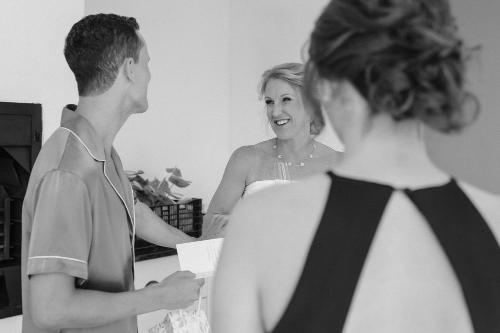 Black and white photo of a smiling woman in a halter dress greeting a man in a casual shirt, with a woman in an updo in the foreground.