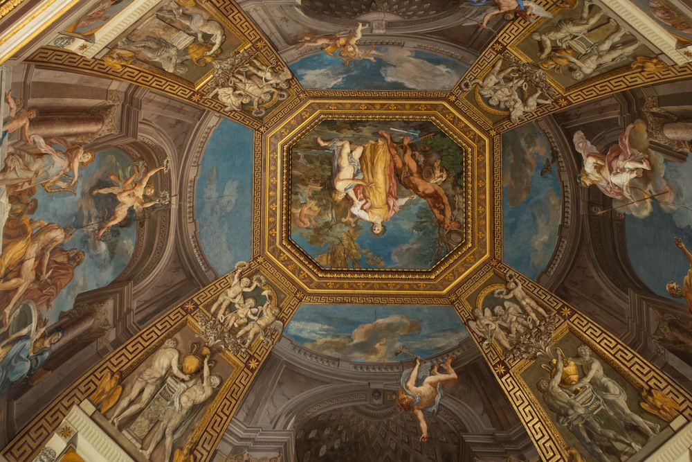 Ornate vaulted ceiling with colorful Renaissance frescoes of angels and figures framed in gold and decorative geometric borders.