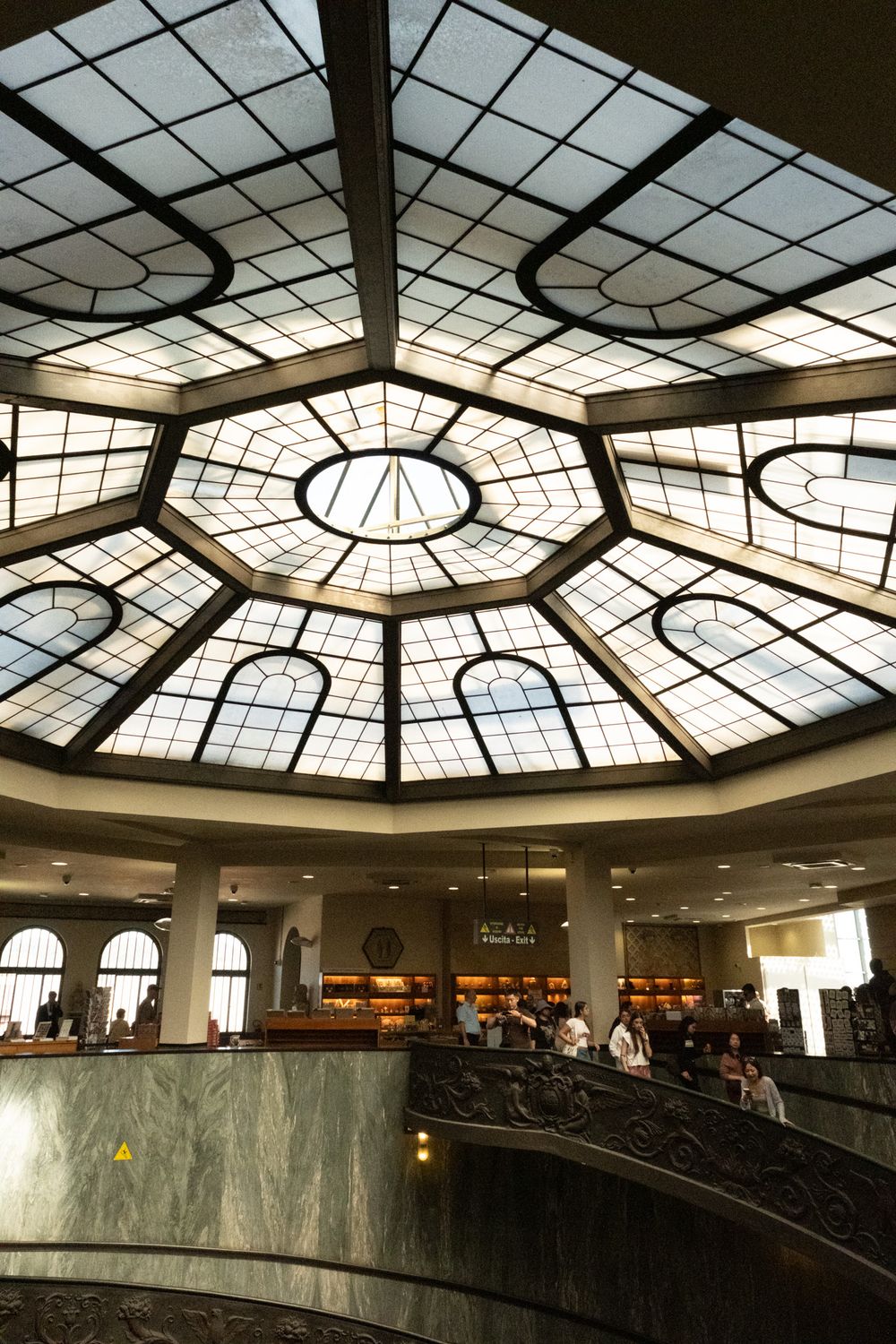 Ornate octagonal glass skylight ceiling above a grand marble staircase and visitors in a spacious, elegant library interior.