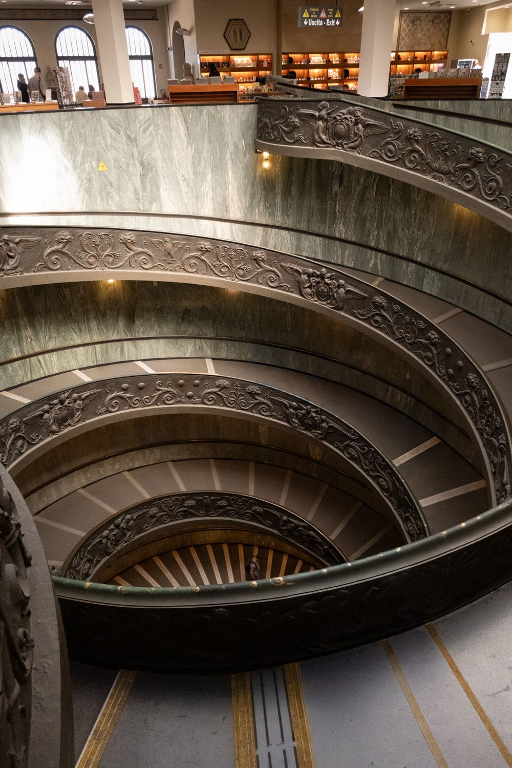 Ornate double helix spiral staircase with bronze balustrades and green marble walls, viewed from above in the Vatican Museums.