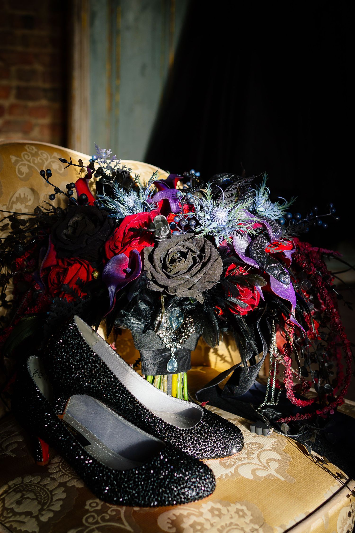 Dark gothic wedding bouquet with red roses, purple calla lilies and a textured black snake by Maddison Rocks, with black glitter bridal shoe