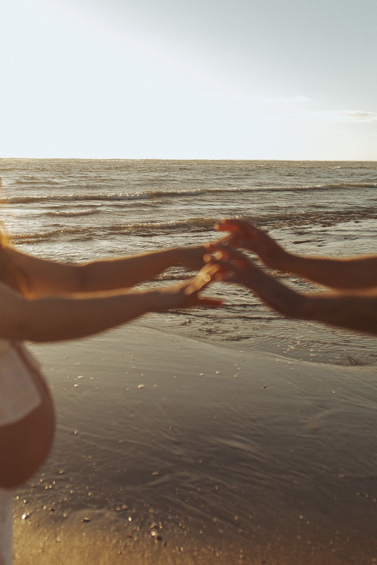 Couple holding hands on a sandy beach at golden sunset with ocean waves in the background during a maternity session in New Zealand, Raglan.
