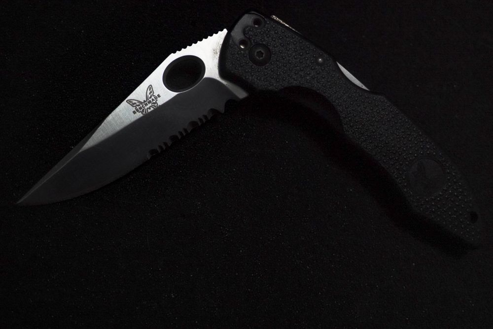 Benchmade folding pocket knife with black handle and partially serrated blade on dark background.