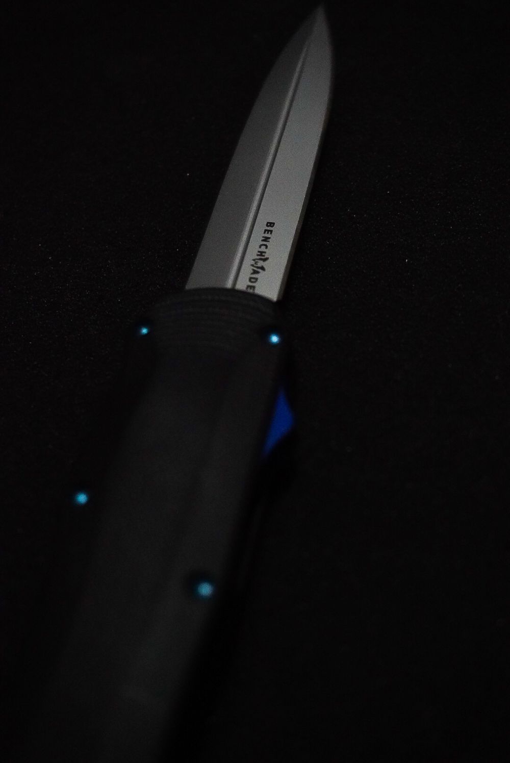 Benchmade tactical knife with black handle and silver blade displayed on dark background with blue accent lights.