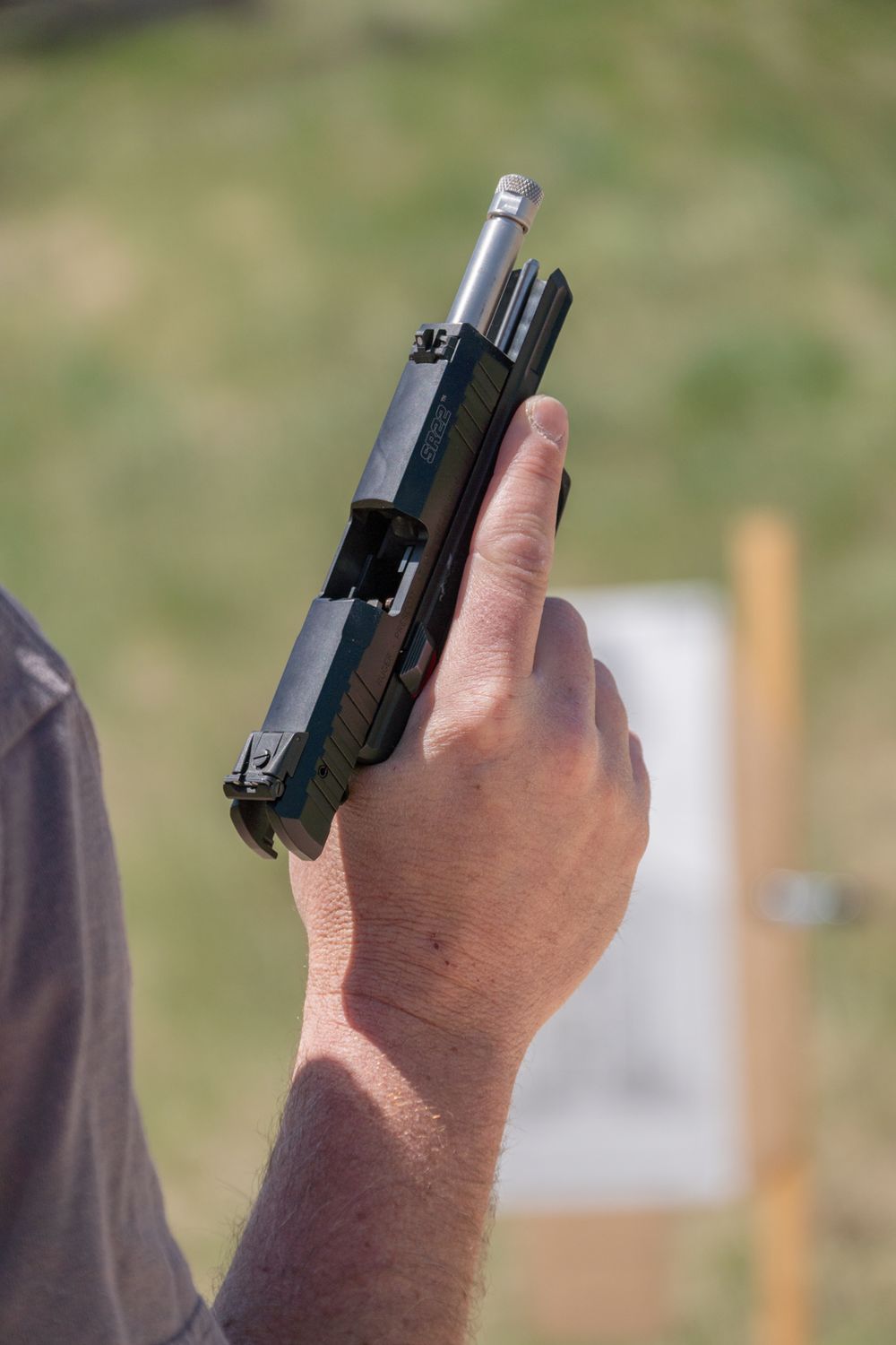 Person holding a semi-automatic pistol at an outdoor shooting range with a white target in the background.