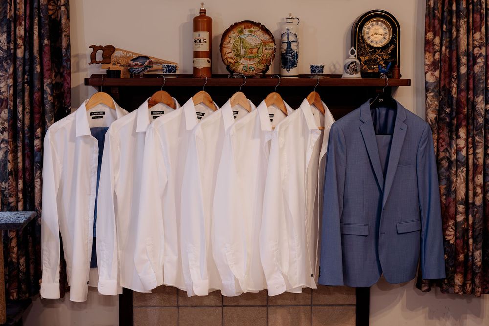 Five white dress shirts and a blue blazer hanging on a rack with decorative shelf above.