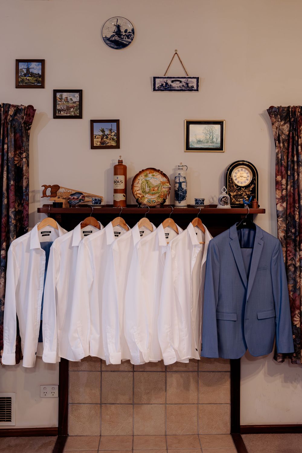 White dress shirts and a blue suit jacket hang on a wooden rack in a decorated room with vintage collectibles and framed art.