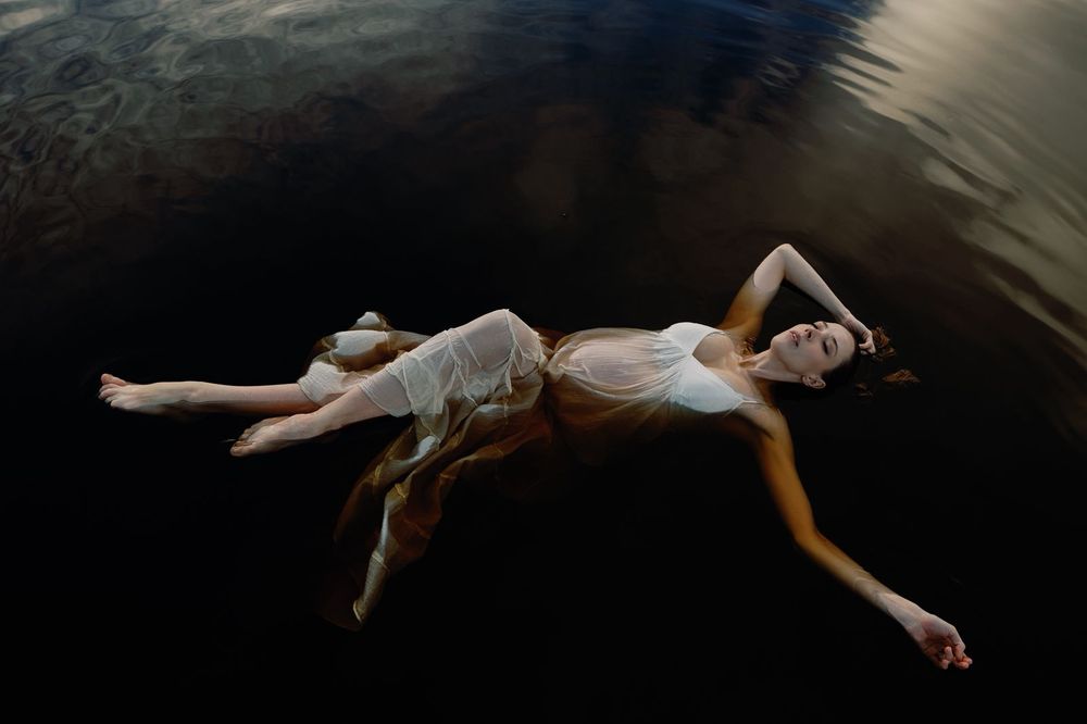 Woman in flowing white dress floating serenely on dark reflective water.