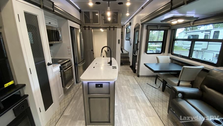 Luxury RV kitchen with white island, stainless appliances, and dining booth seating area.