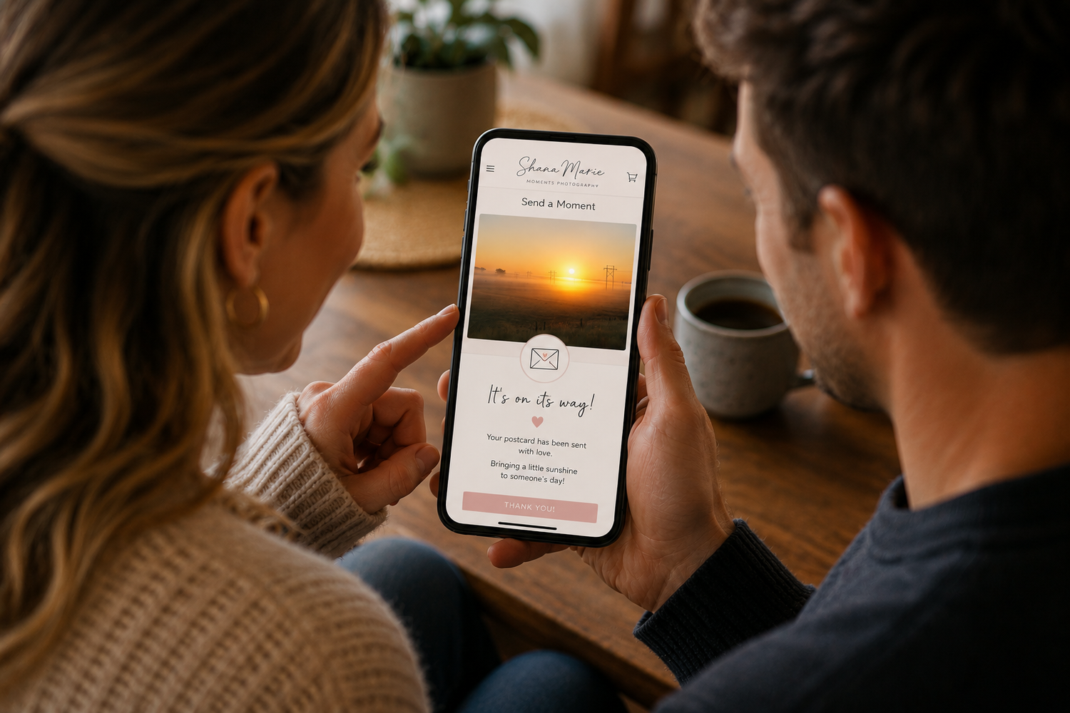 Couple viewing a wedding invitation app on a smartphone with a sunset photo displayed on screen.