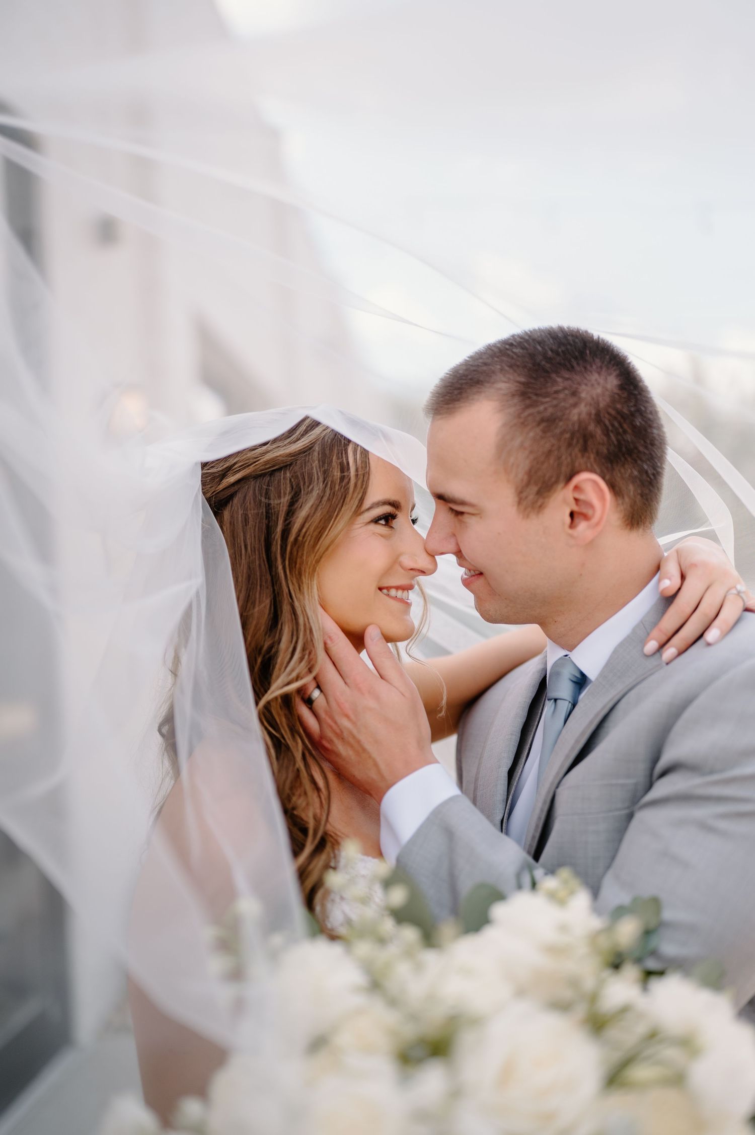 Bride and groom sitting closely on stone steps outside elegant venue, sharing an intimate moment in wedding attire.