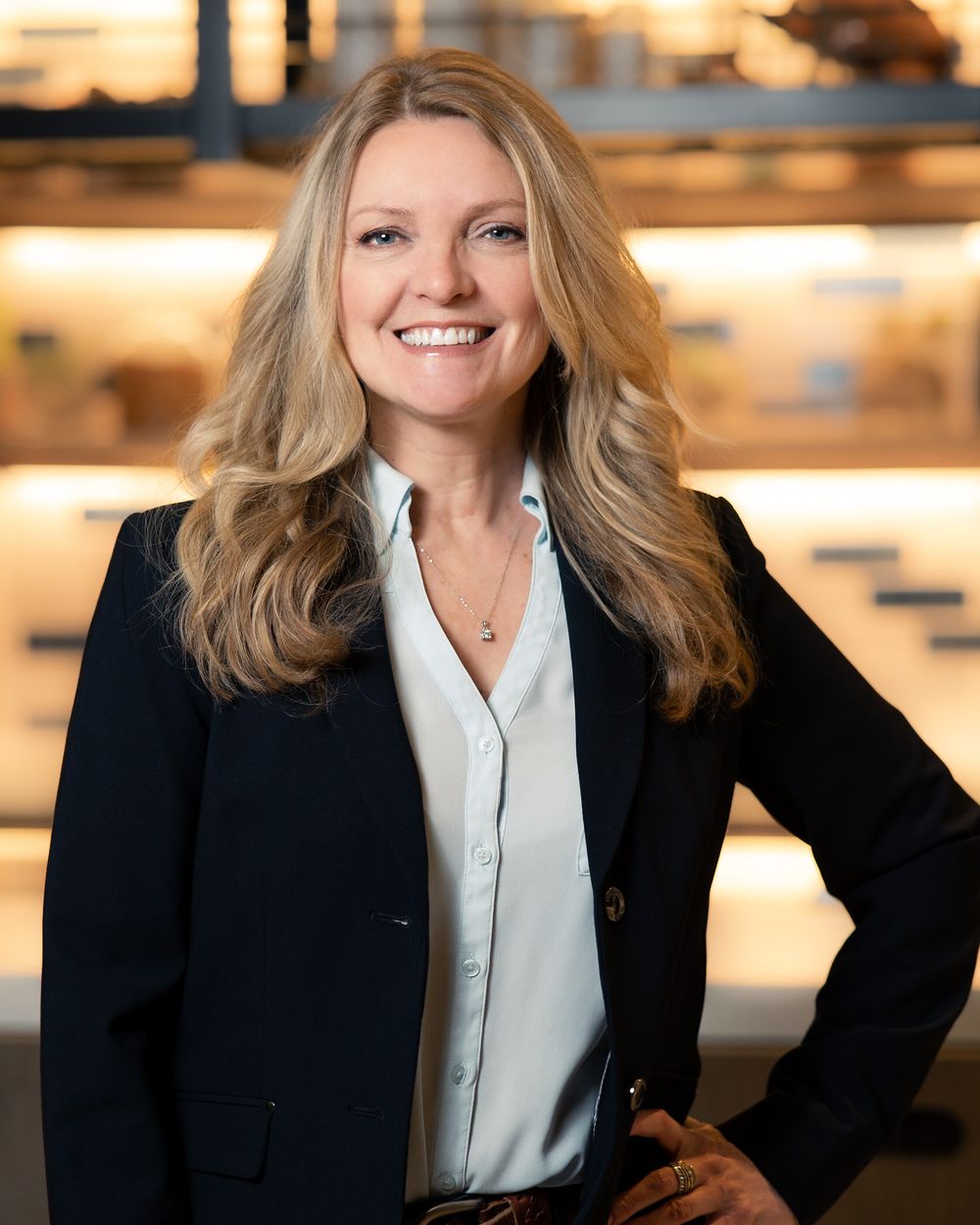 Professional businesswoman in navy blazer and light blue blouse smiling confidently in modern office setting.