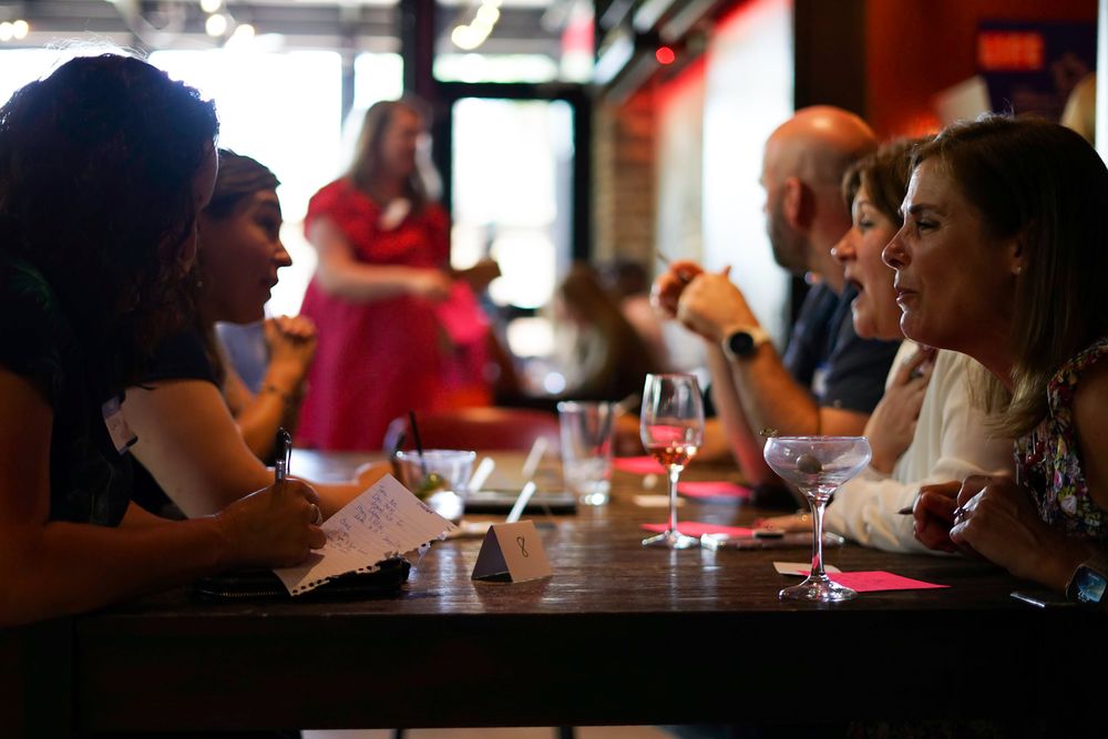 People socializing at a restaurant bar, enjoying wine and conversation at a dimly lit wooden table.
