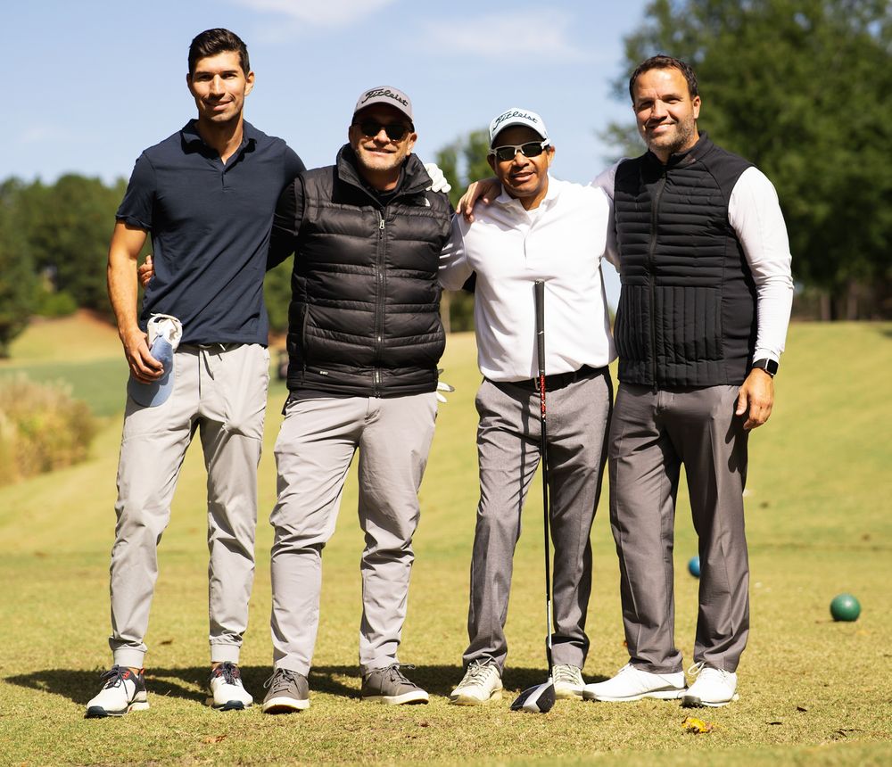 Four men posing together on a golf course, smiling and dressed in casual golf attire on a sunny day.