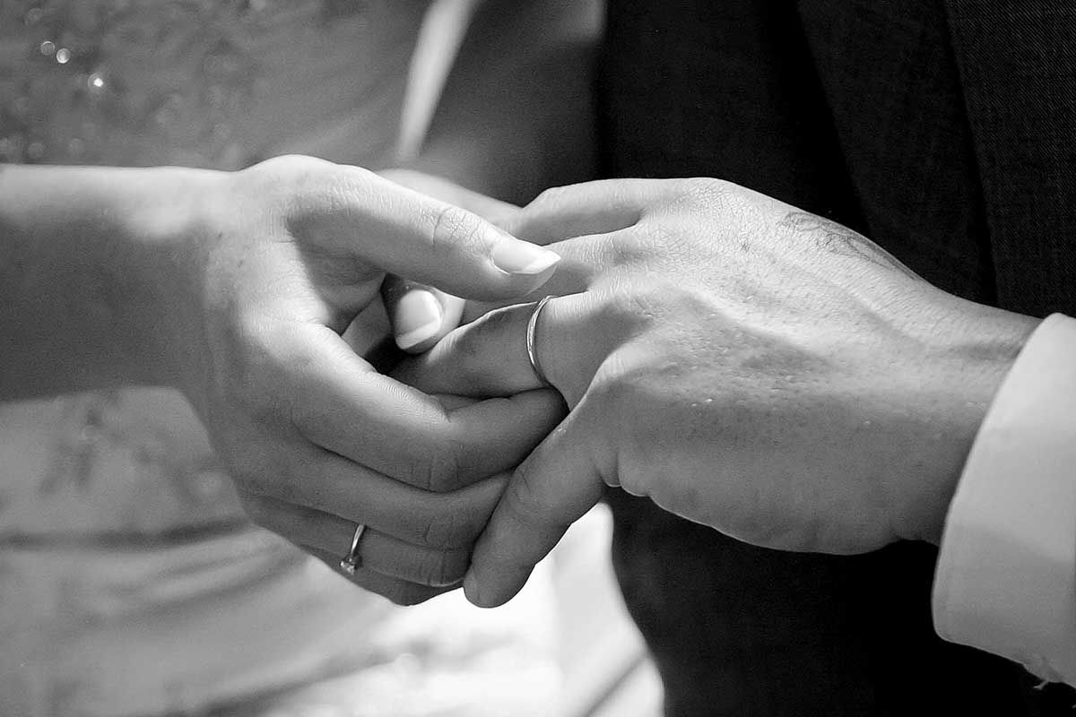 Black and white photo of a couple exchanging wedding rings during a marriage ceremony.