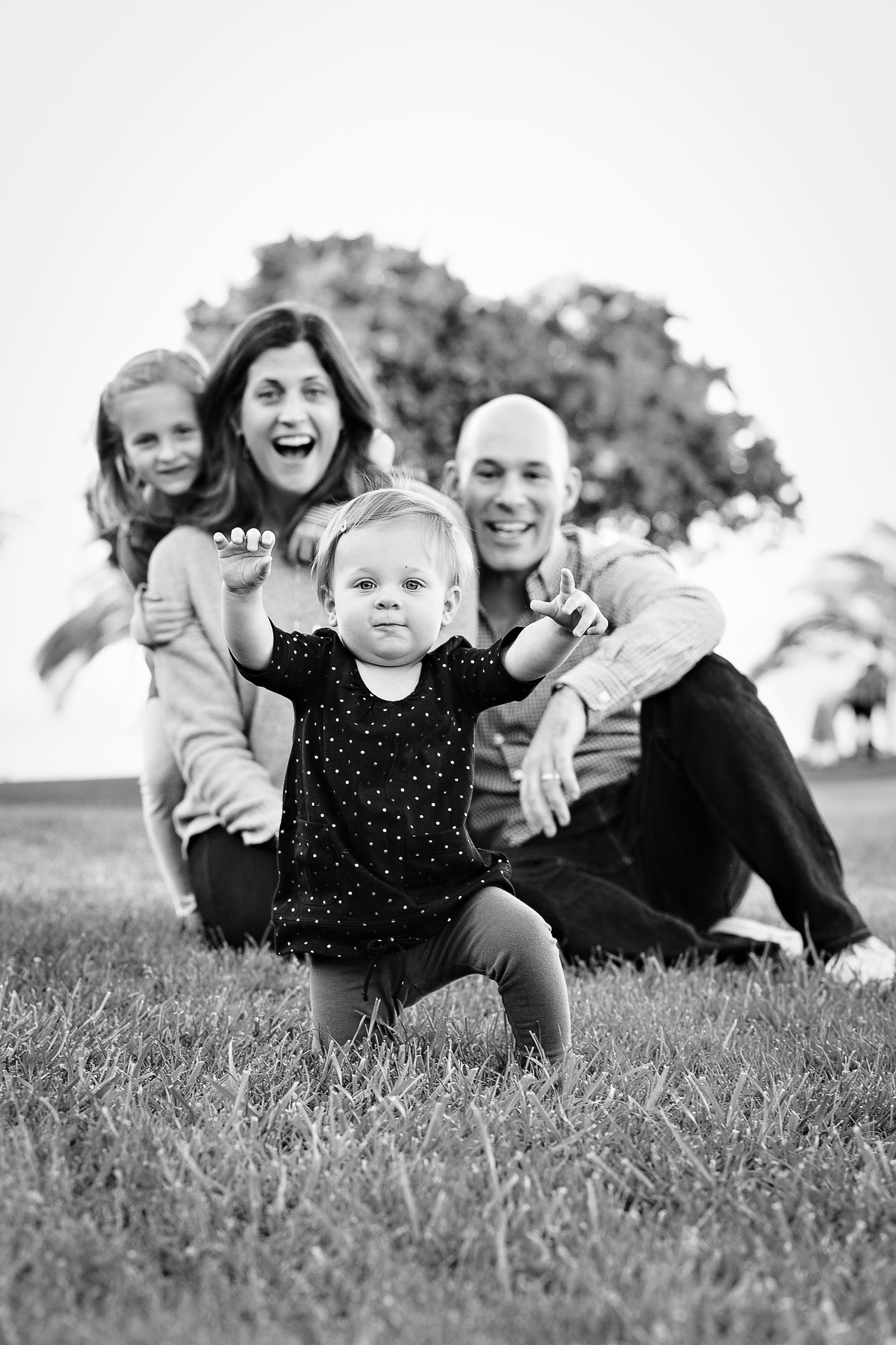 Black and white family portrait of five smiling people sitting together outdoors on a bridge deck.