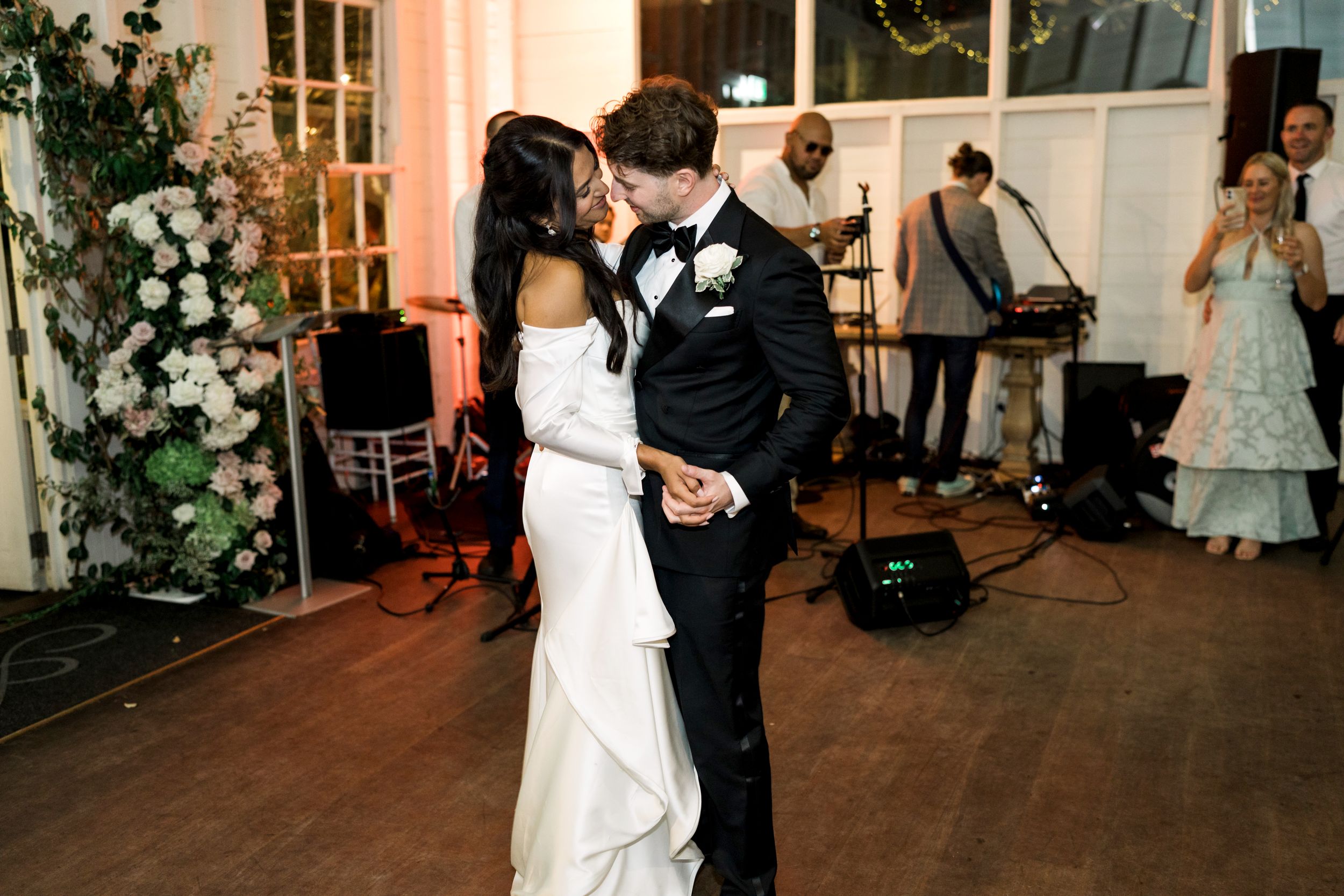 A bride and groom share their first dance kiss at an elegant wedding reception with a live band performing in the background.
