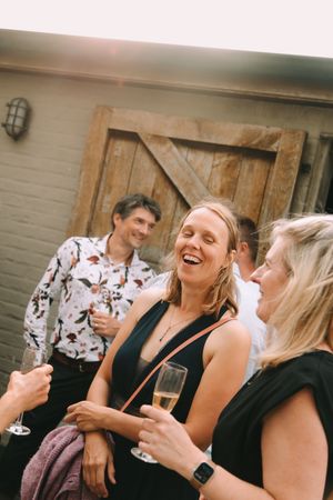 Vrienden lachen samen met een glas champagne tijdens de receptie van een intiem trouwfeest in Deinze.