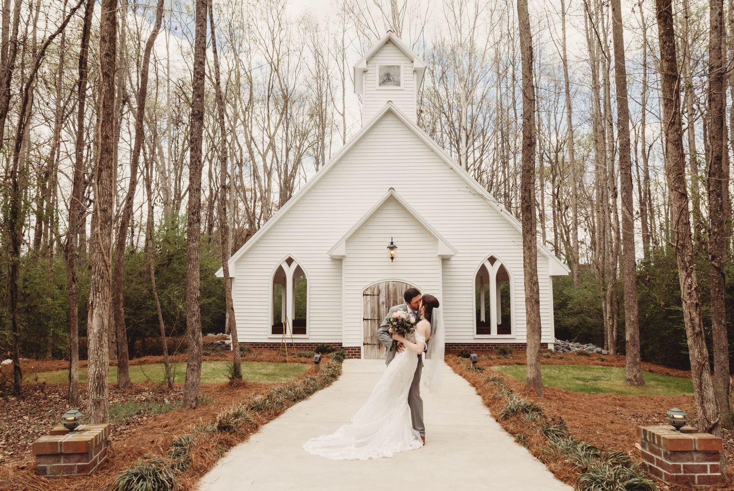 Military groom in dress uniform walks with bride in white gown through ornate iron garden gate on wedding day.