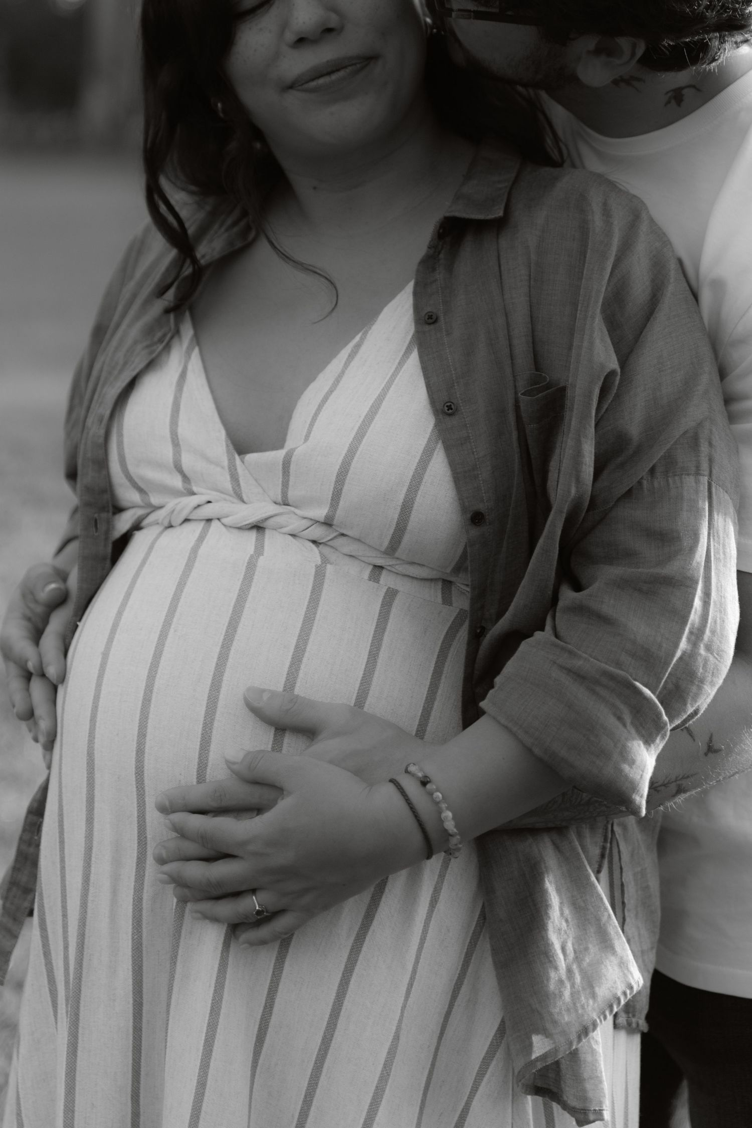 Black and white close-up of pregnant woman in striped dress with partner gently holding her baby bump.