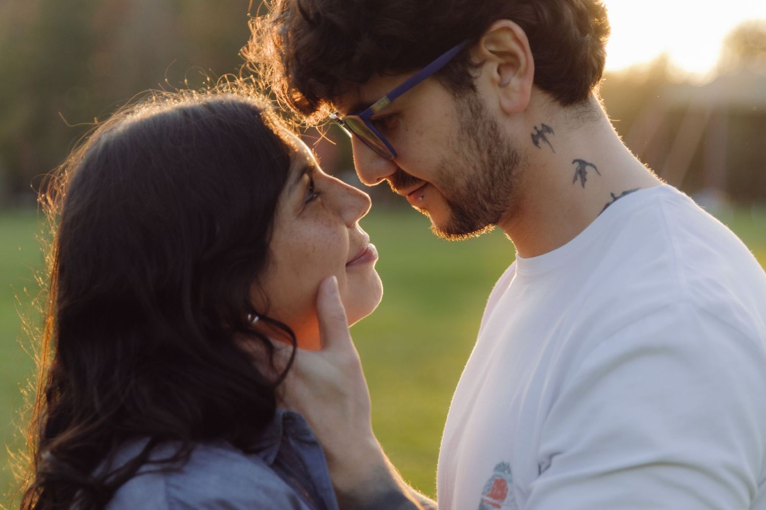 A couple shares a romantic moment, almost kissing, with golden sunset light in a park.