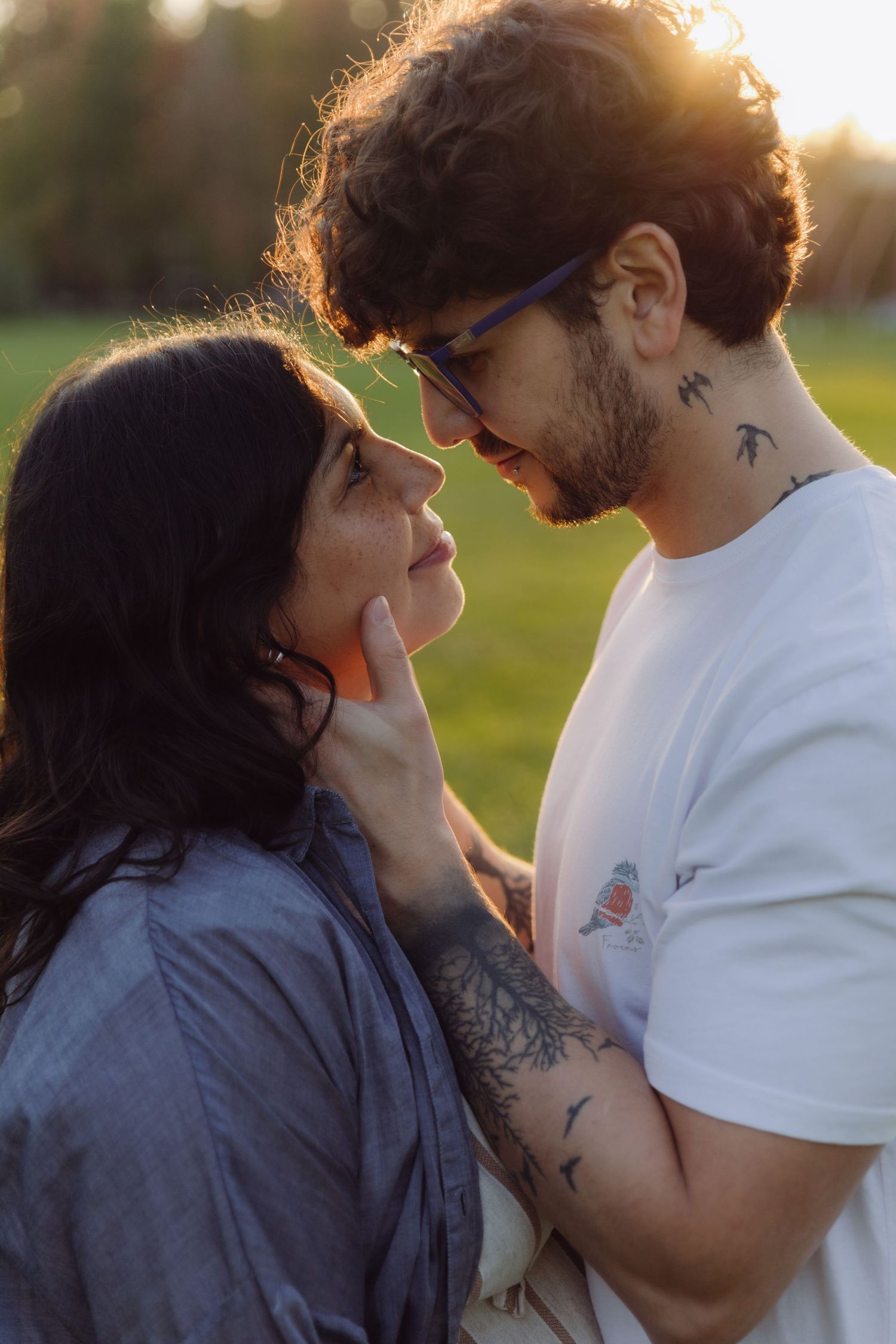 Tattooed couple sharing intimate moment face to face at golden hour outdoors.