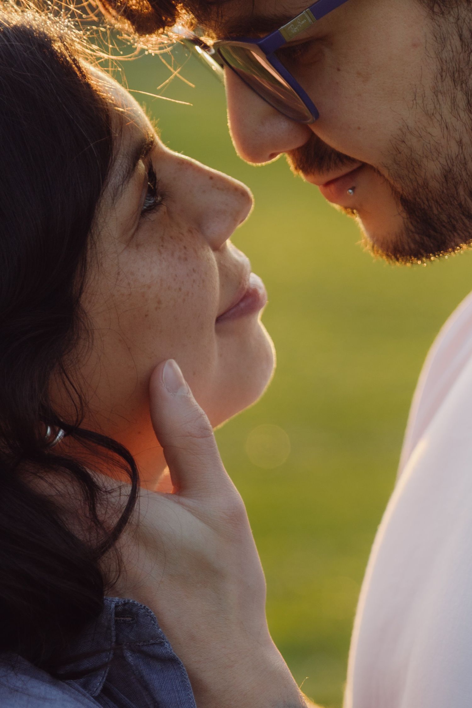 Romantic couple sharing an intimate moment outdoors at golden hour, man with beard and glasses gently touching womans face.