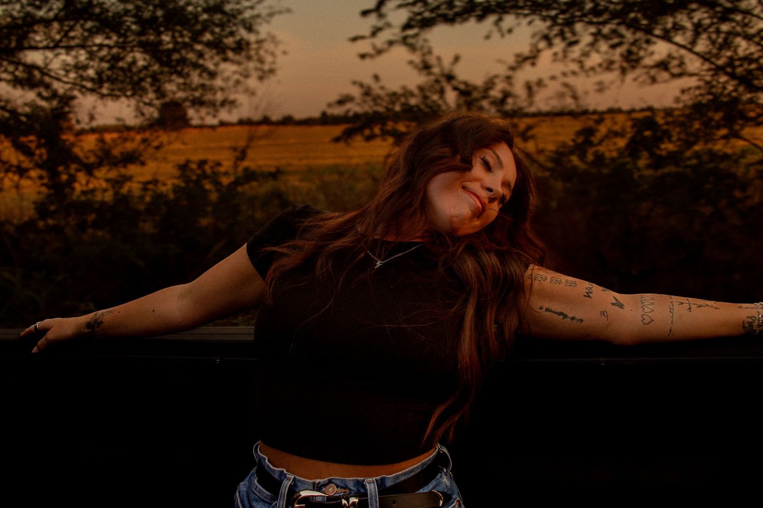 Woman posing outdoors at sunset during a warm, cinematic golden hour portrait session in Oklahoma.