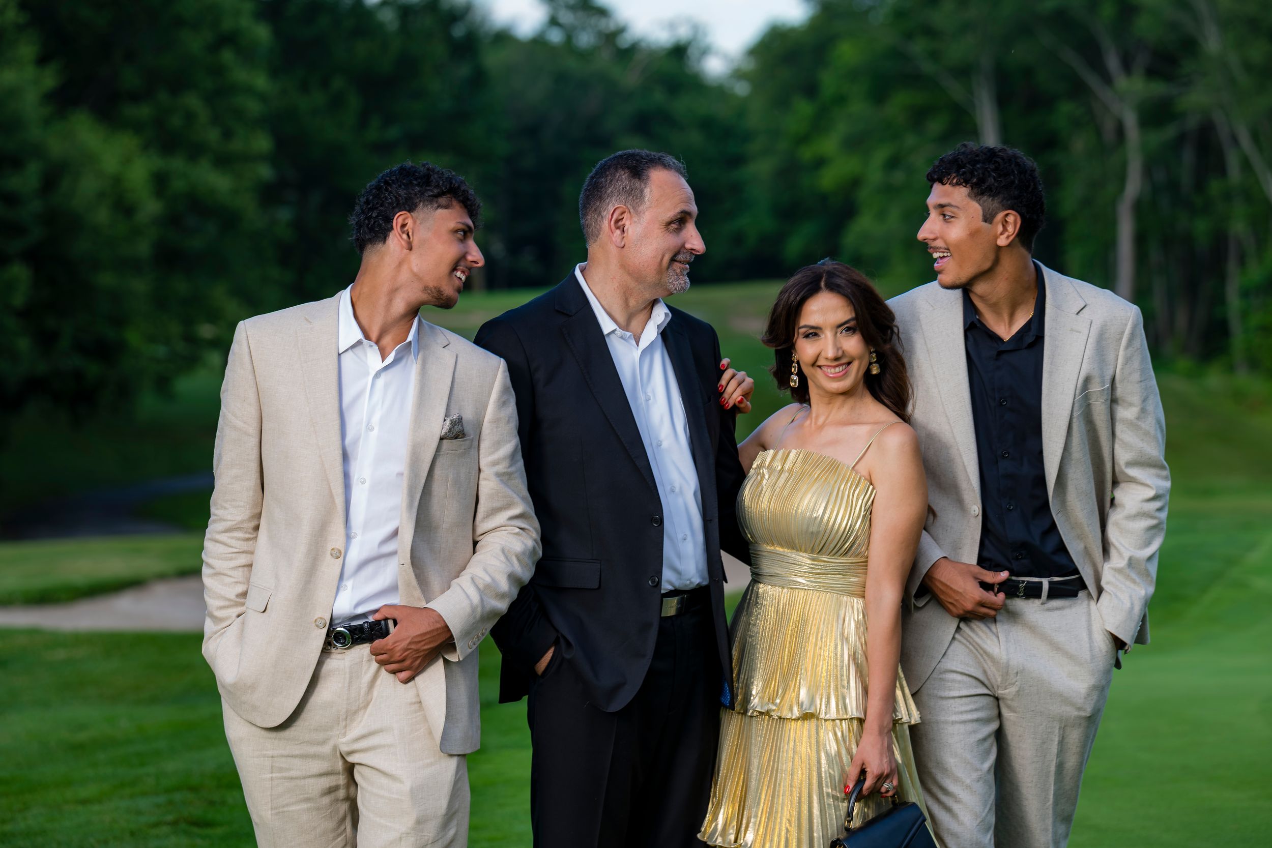 Family of four posing outdoors on a golf course, dressed in elegant formal attire for a special occasion.