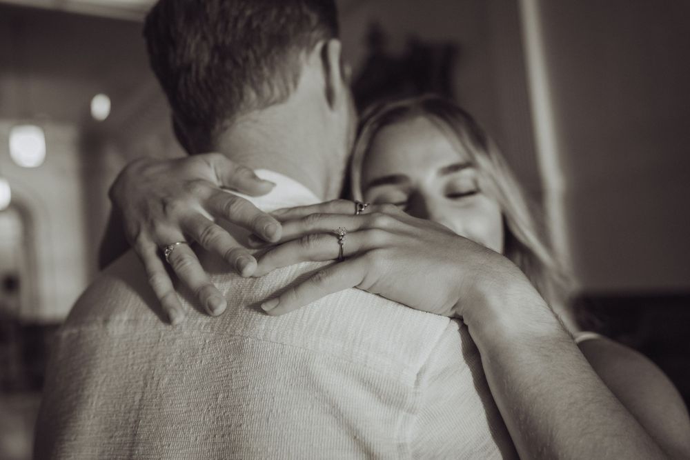 Black and white photo of a couple sharing a tender embrace, woman with eyes closed hugging man warmly.