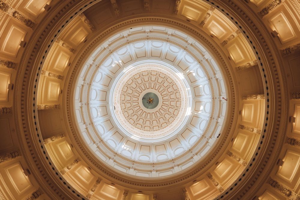 Interior view of an ornate golden capitol building rotunda dome with intricate architectural details and skylight.