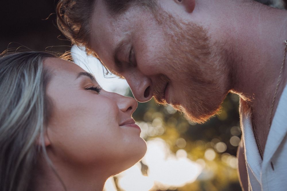 Romantic couple sharing an intimate moment, nearly kissing outdoors in warm golden sunlight.