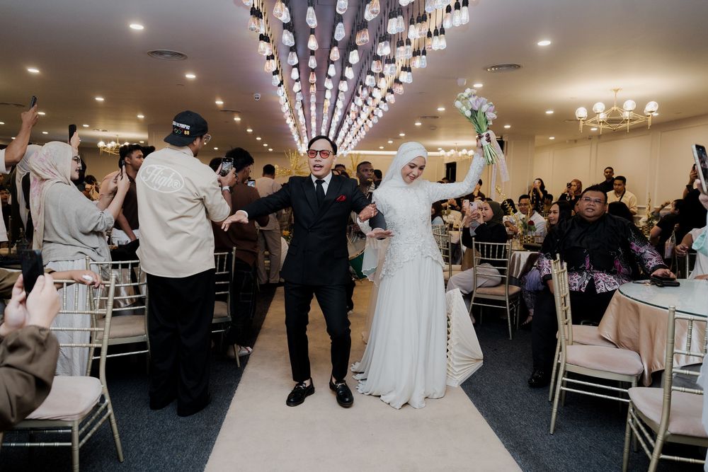 Muslim bride and groom celebrate their wedding reception entrance in an elegant banquet hall with guests applauding.
