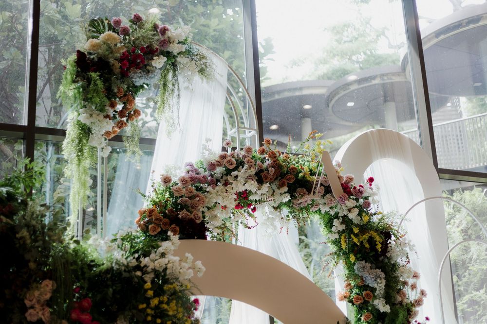 Elegant wedding arch adorned with lush greenery and colorful flowers in a sunlit venue.