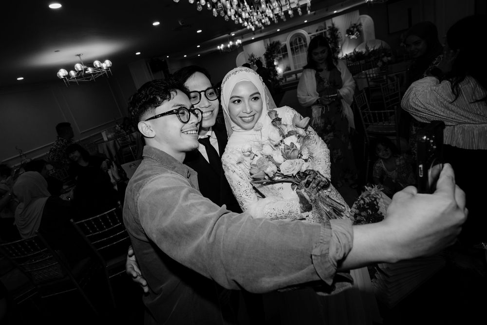 Wedding guests taking selfie with bride in hijab at reception.