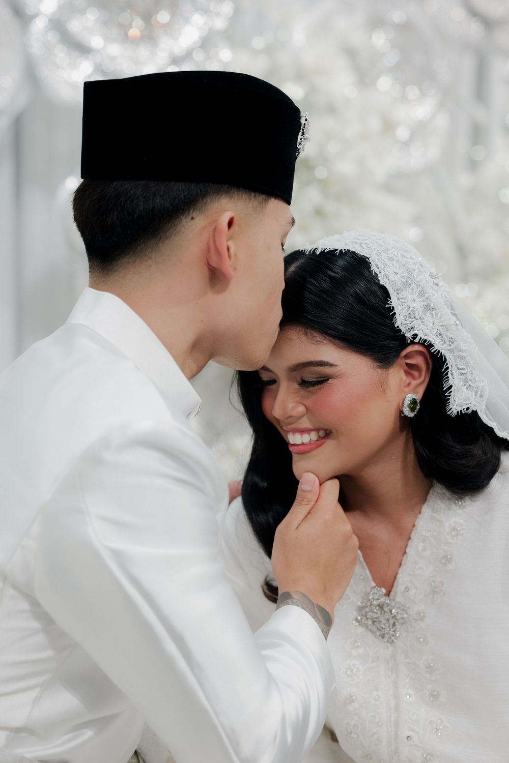 A couple in traditional Malay wedding attire sharing an intimate moment, groom in white baju melayu and songkok.