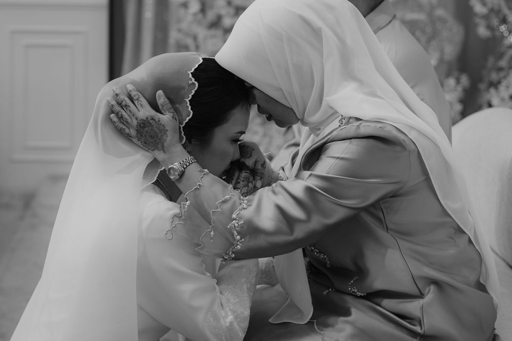 Black and white photo of two women in hijabs sharing an emotional embrace at a wedding ceremony.