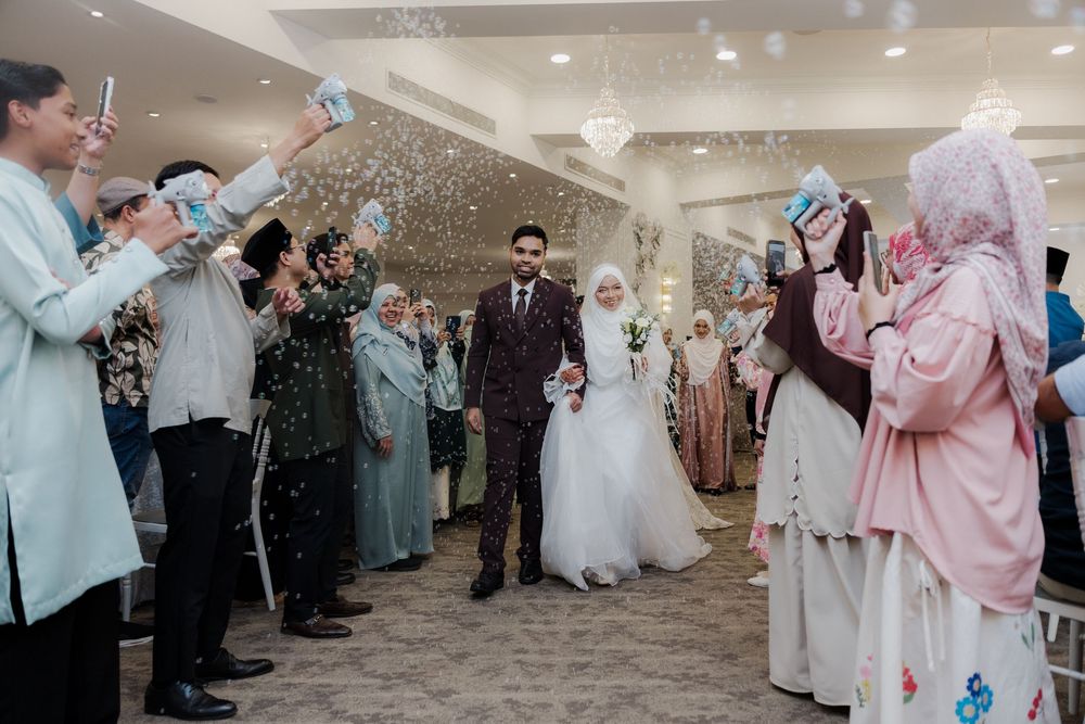 Muslim bride and groom walk through cheering guests throwing confetti at an elegant indoor wedding celebration.