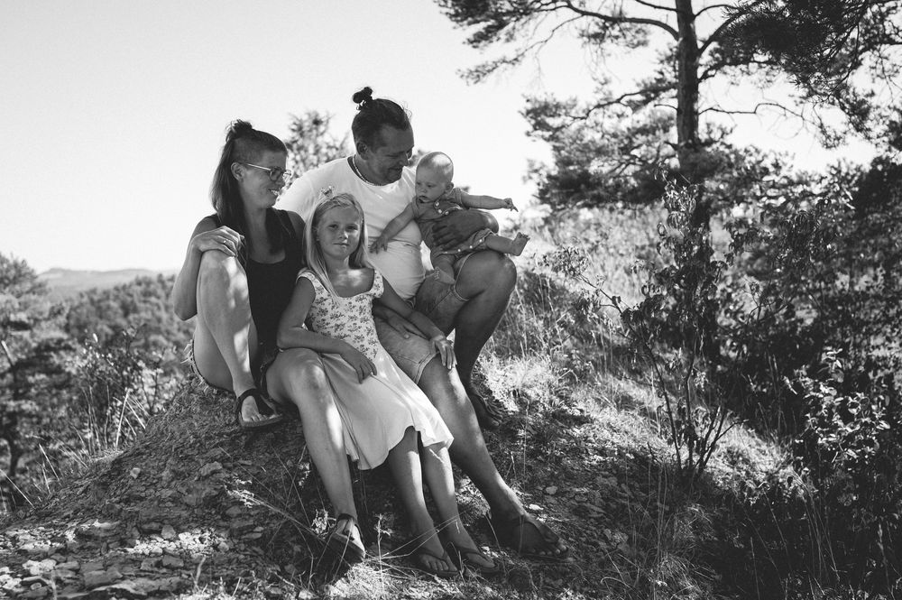 Black and white photo of a happy family sitting together on a rocky hillside surrounded by trees on a sunny day.