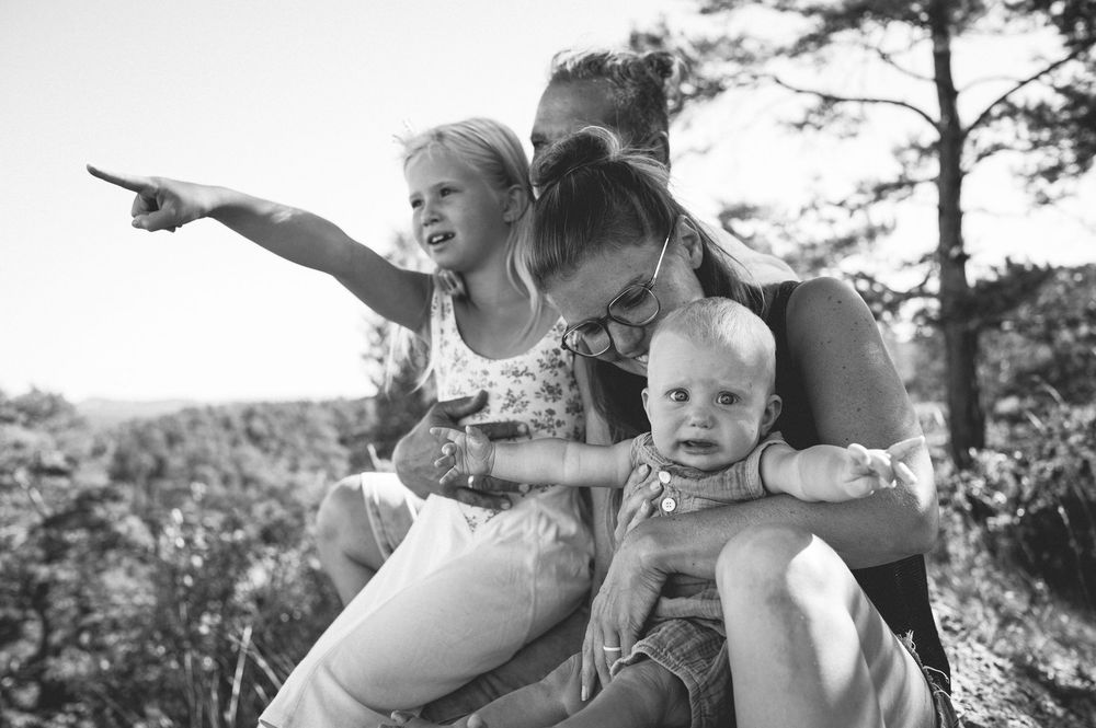 Black and white photo of a family outdoors, with a young girl pointing into the distance while parents hold a baby.