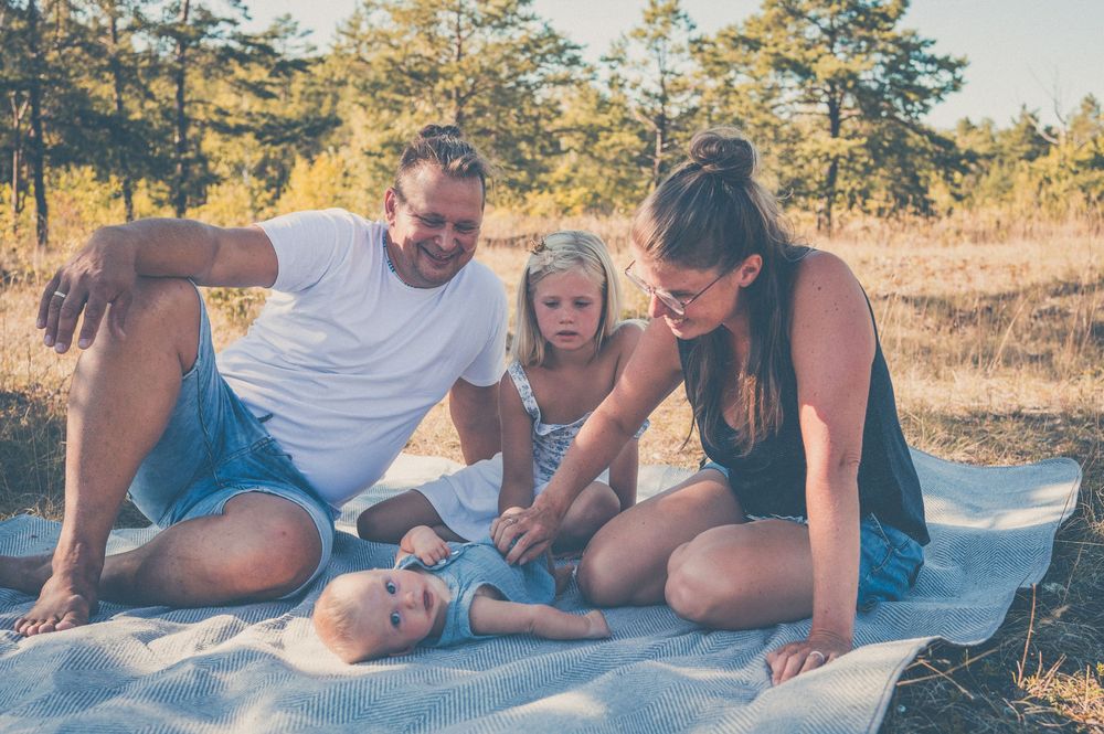 Family of four enjoying a sunny outdoor picnic on a blanket surrounded by trees.