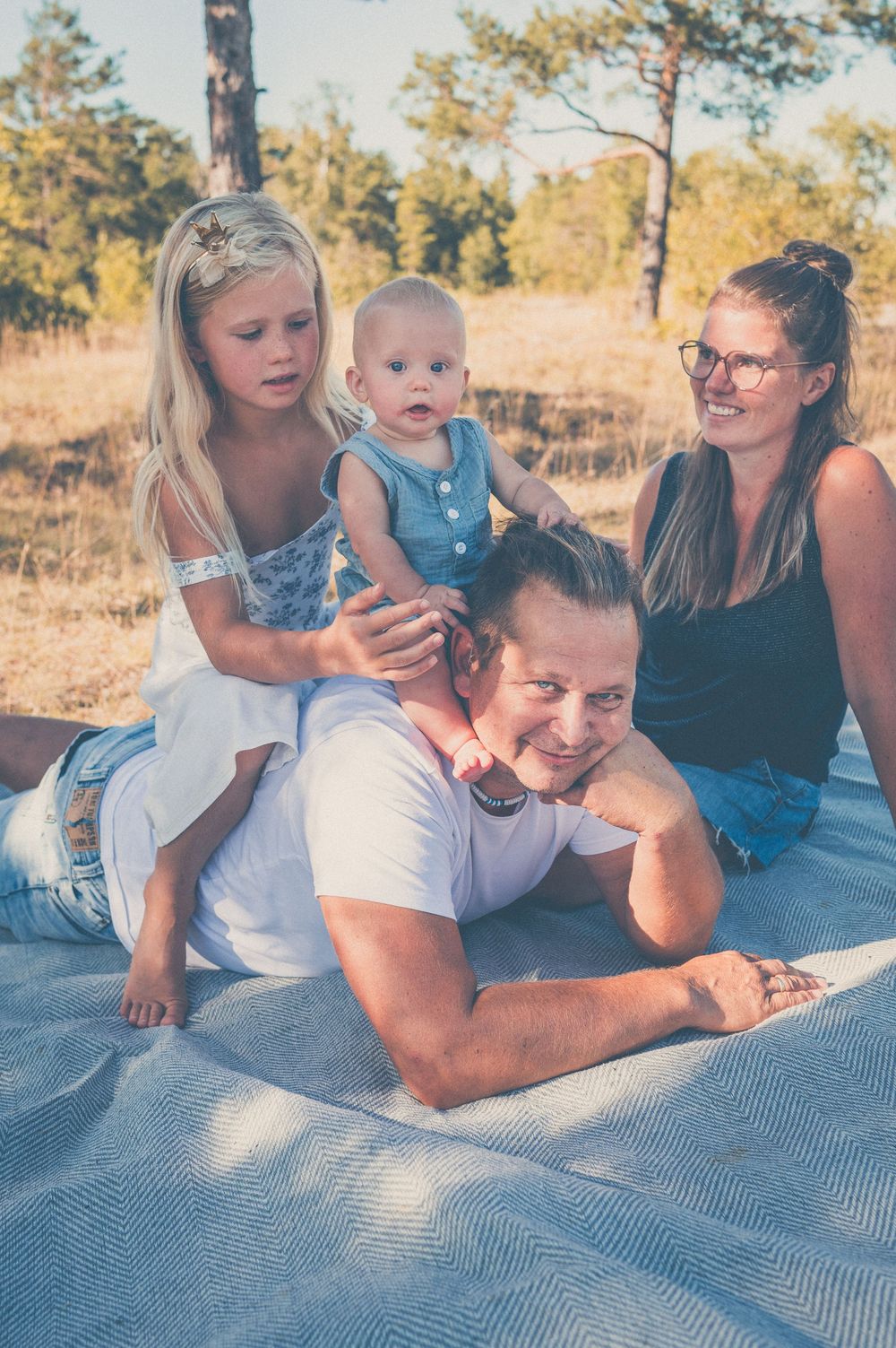 Family of four relaxing on a blanket outdoors, with parents and two young children enjoying a sunny day in nature.