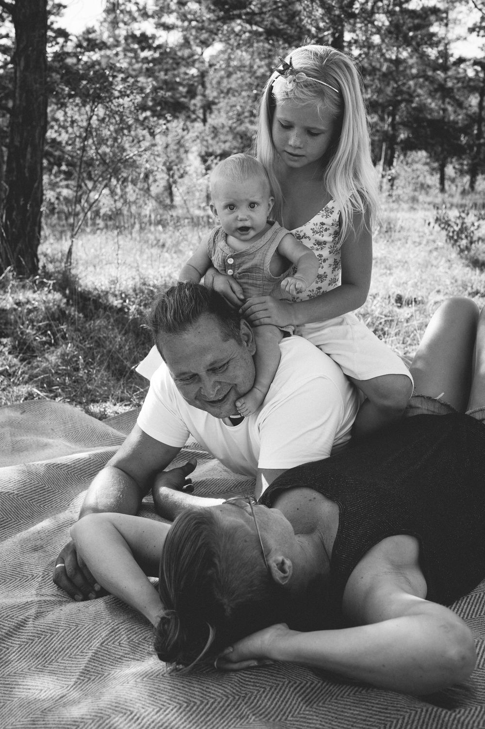 Black and white family photo of a man, baby, and girl relaxing on a blanket outdoors in a forest setting.