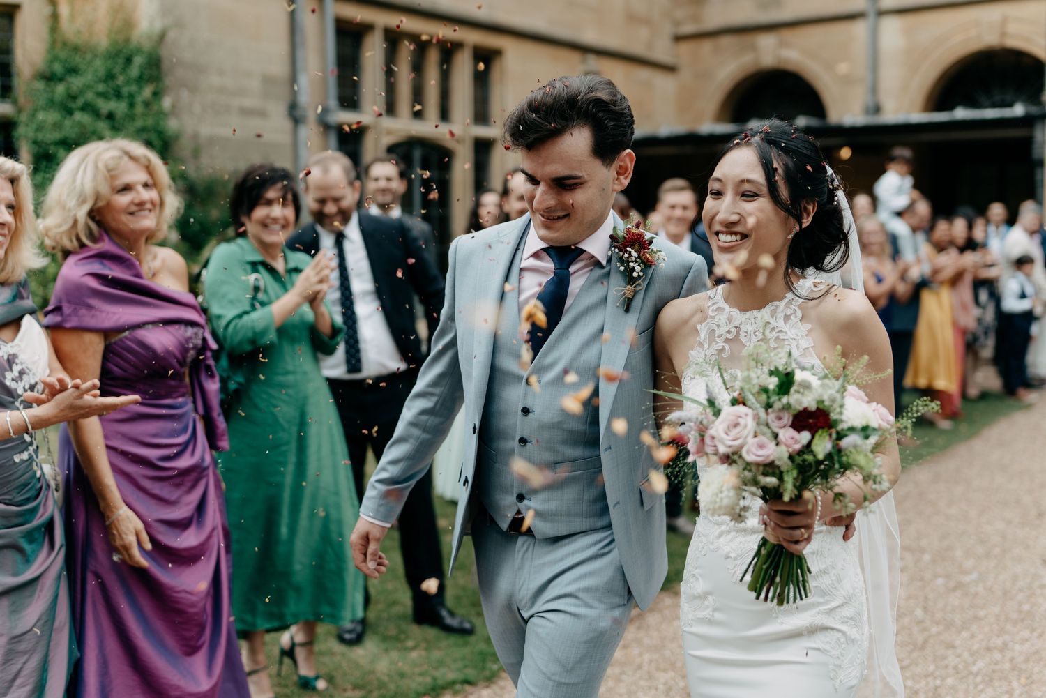 A joyful bride and groom walk through a confetti shower surrounded by cheering guests.
