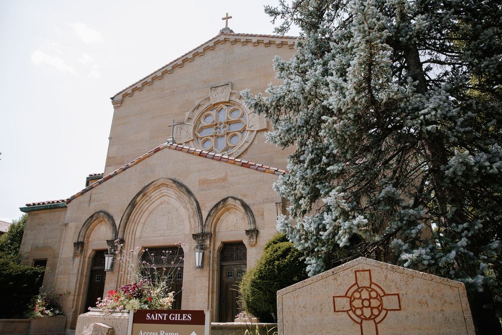 Exterior view of Saint Giles Catholic Church featuring Romanesque architecture, rose window, arched entries, and a Celtic cross monument.