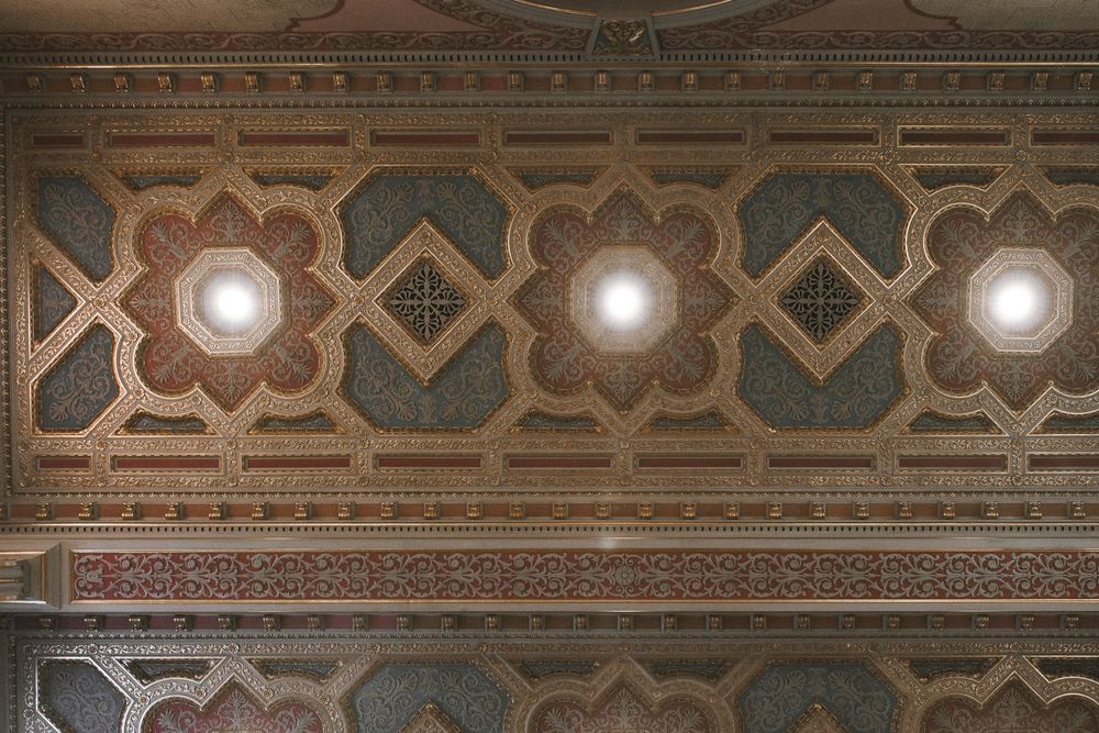 Ornate ceiling with geometric patterns, floral motifs, and glowing lights in a historic architectural interior.