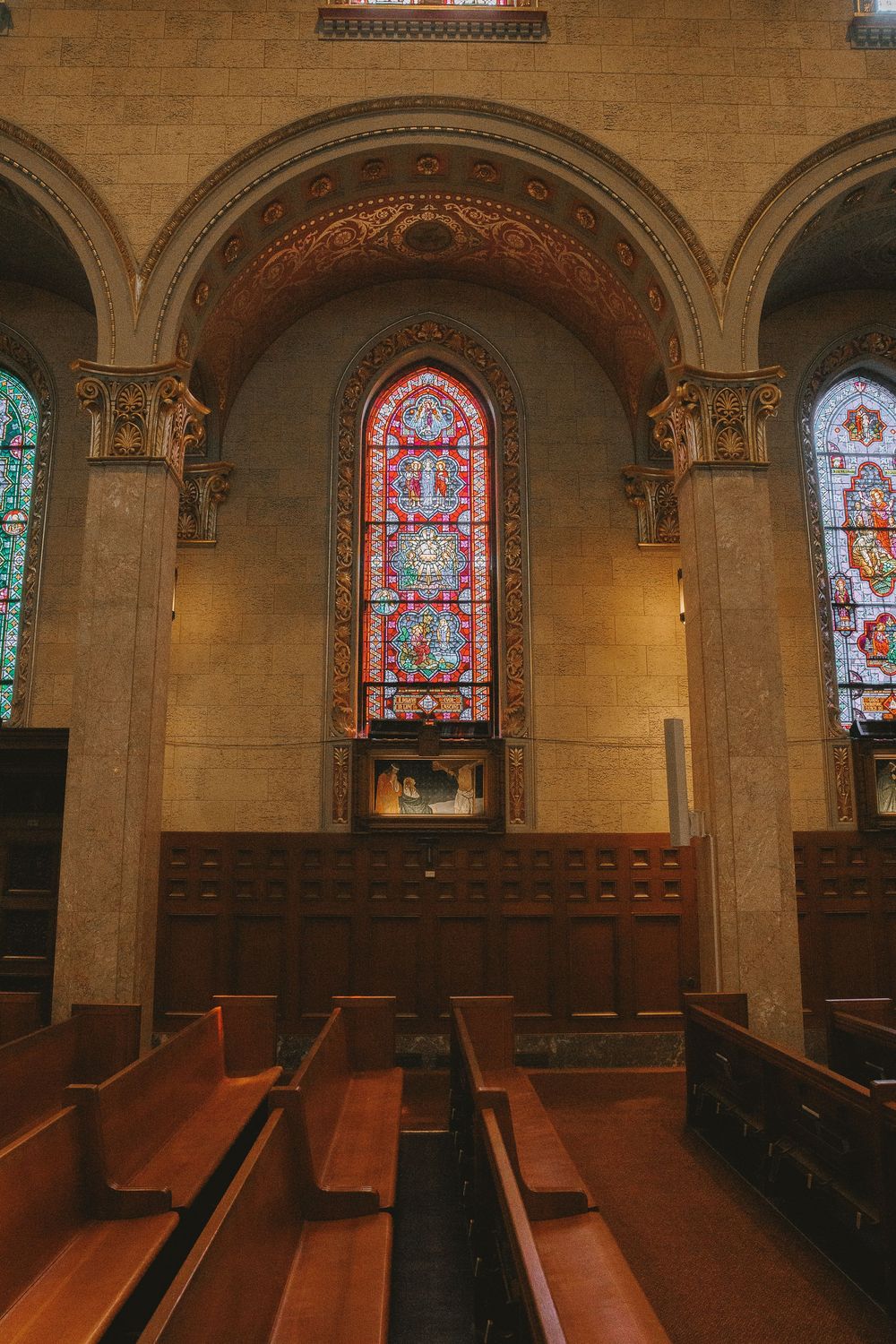 Interior of a historic church featuring wooden pews, stone arches, and colorful stained glass windows.