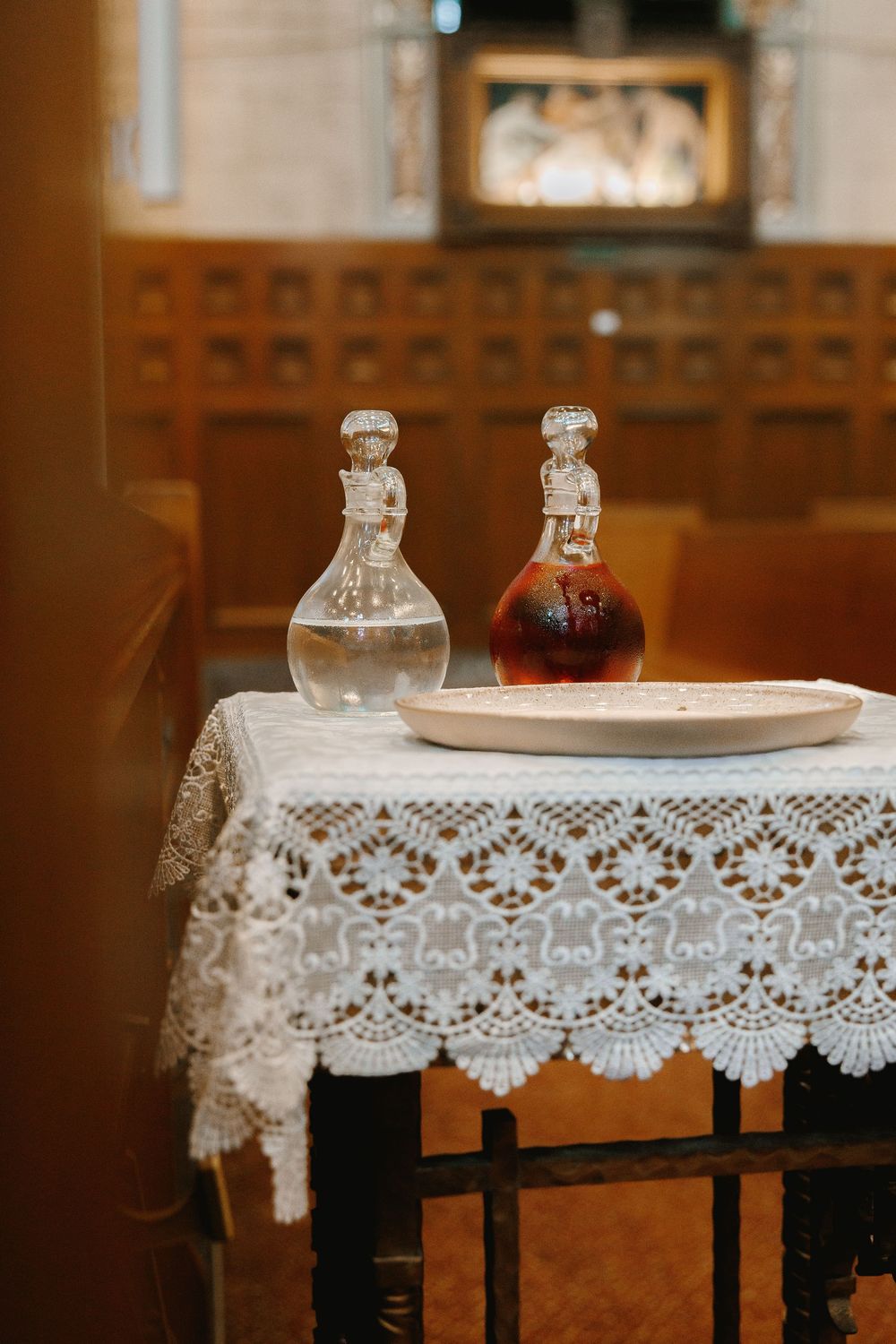 Two ornate glass decanters on a lace-covered table inside a church during a wedding ceremony.