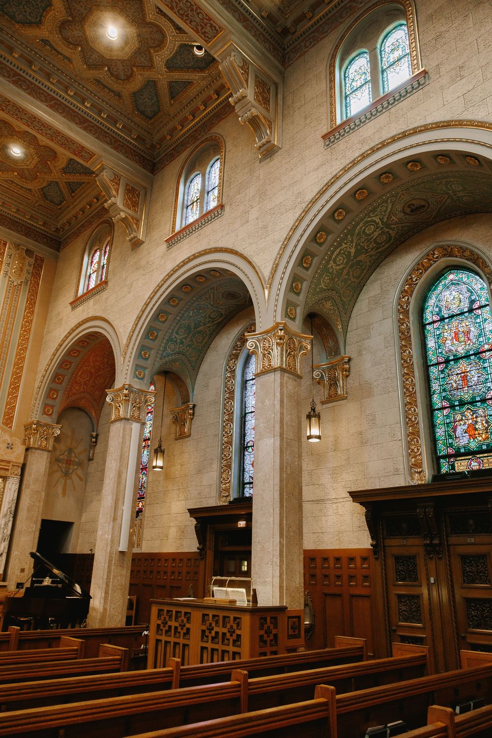 Grand church nave with arched columns, colorful stained glass windows, and ornate ceiling details.